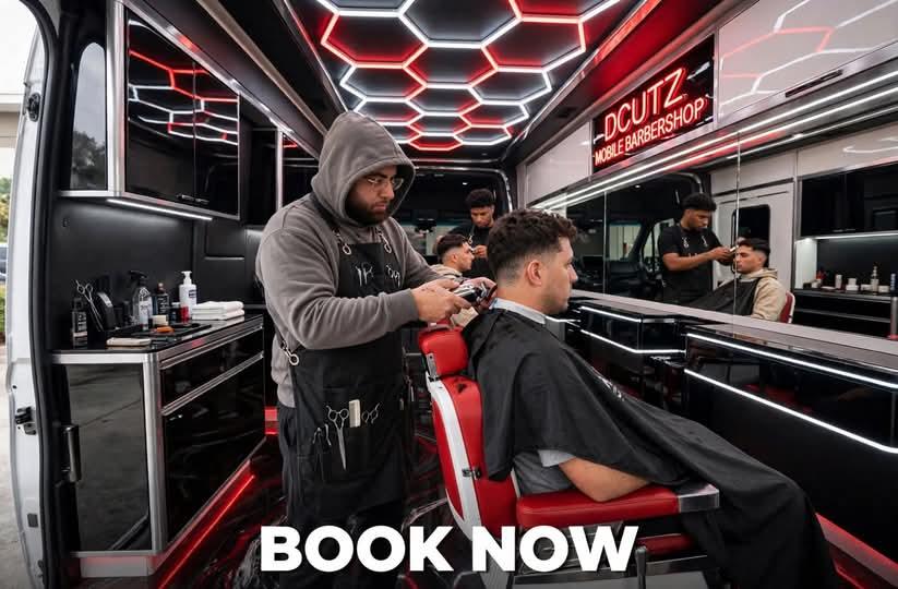 Barber working on a client with the mirror wall and neon DCUTZ sign behind them