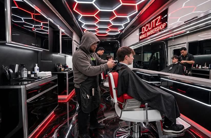 A barber giving a client a haircut in the van while another barber works in the mirror